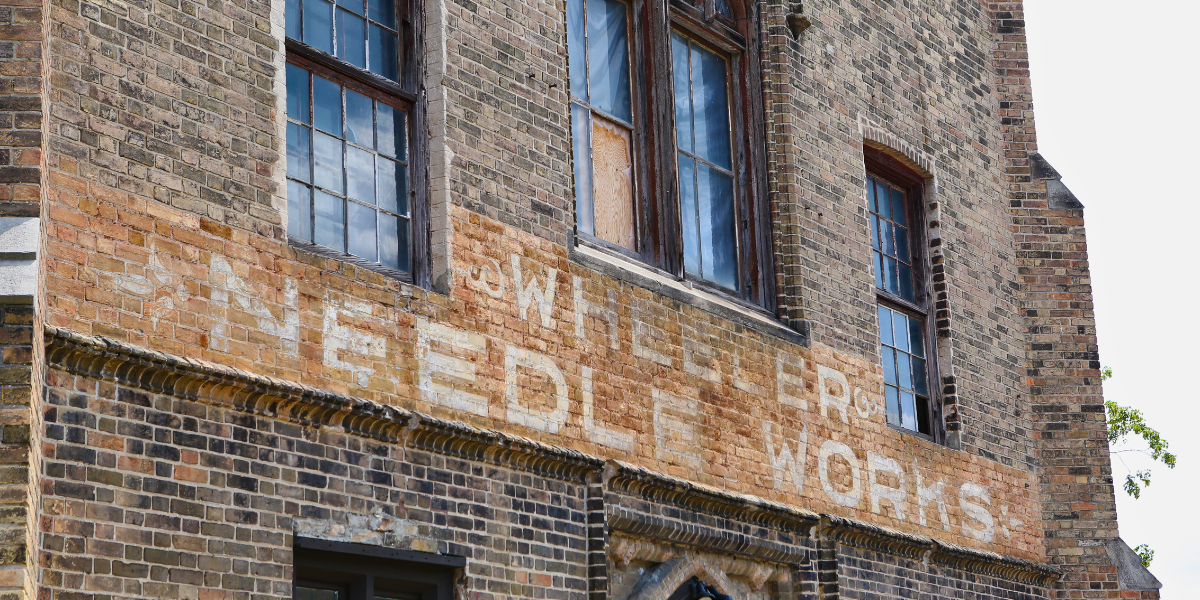 Painted Wheeler Needle Works sign on the front exterior of the Bawcutt Centre building.