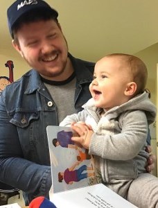 father holding his smiling baby who is holding a board book